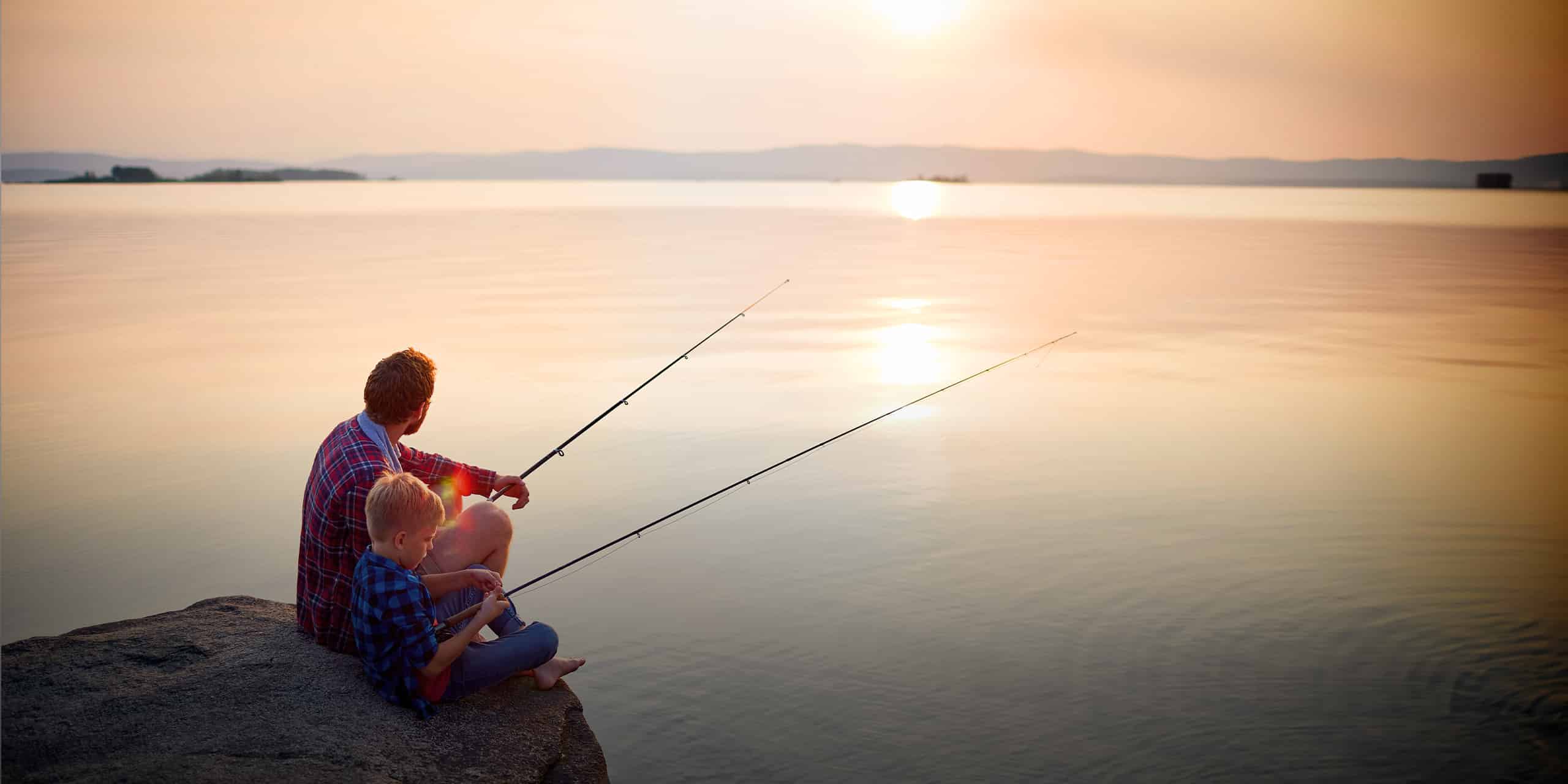 Father and son fishing at calm lake in setting sun.