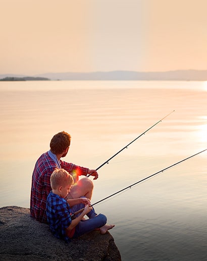 Father and son fishing at calm lake in setting sun.